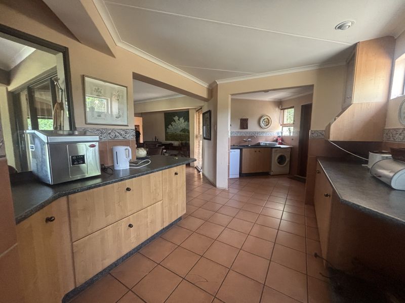 Open-plan kitchen featuring light wood cabinetry, dark laminate countertops, and terracotta floor tiles, with an adjoining scullery area.
