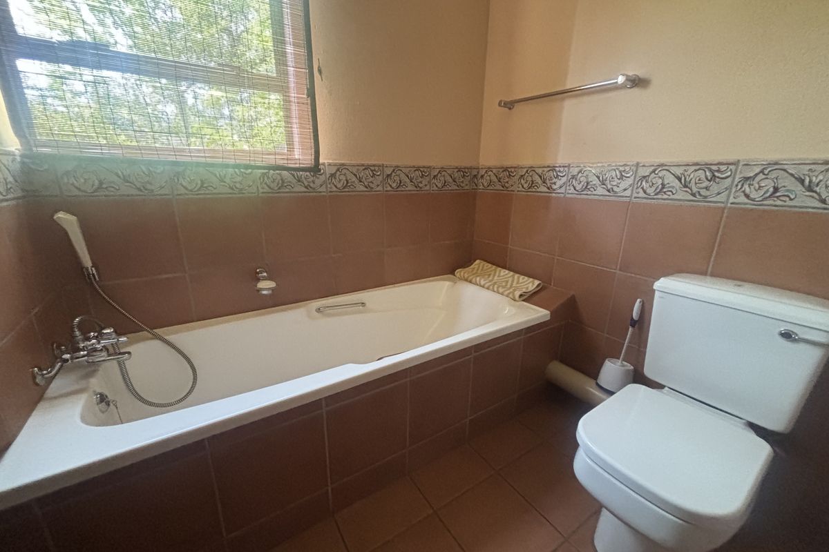 A functional bathroom featuring a built-in bathtub with shower attachment, a standard toilet, and decorative wall tiling.