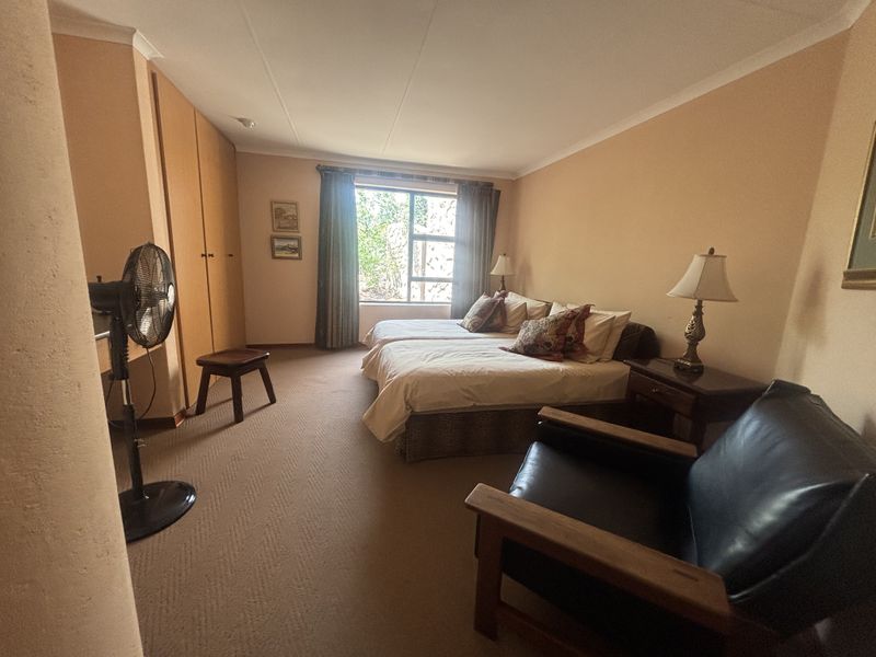 A spacious bedroom featuring built-in wooden cupboards, neutral carpeting, and a large window providing natural light.