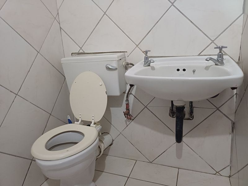 A compact bathroom featuring tiled walls and floors, a wall-mounted basin, and a standard toilet suite with exposed plumbing fixtures.