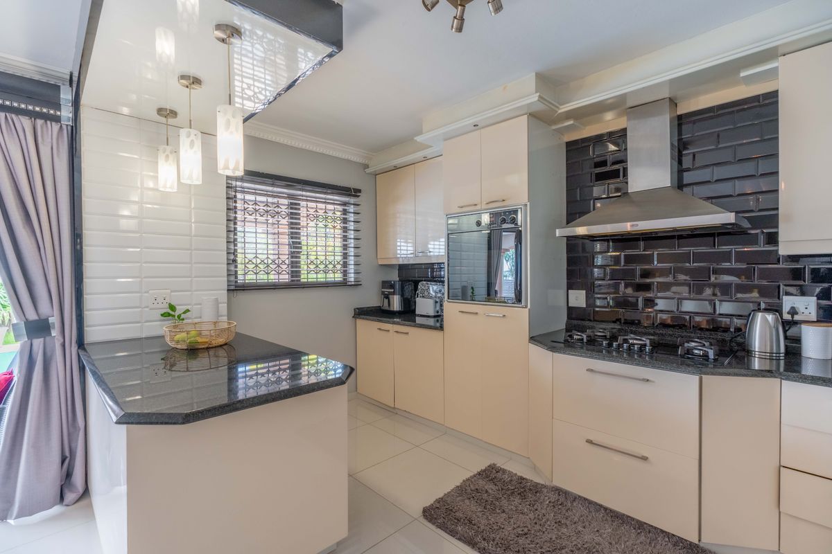 Modern kitchen featuring granite countertops, built-in oven, gas hob with stainless steel extractor, and stylish subway tile backsplash.