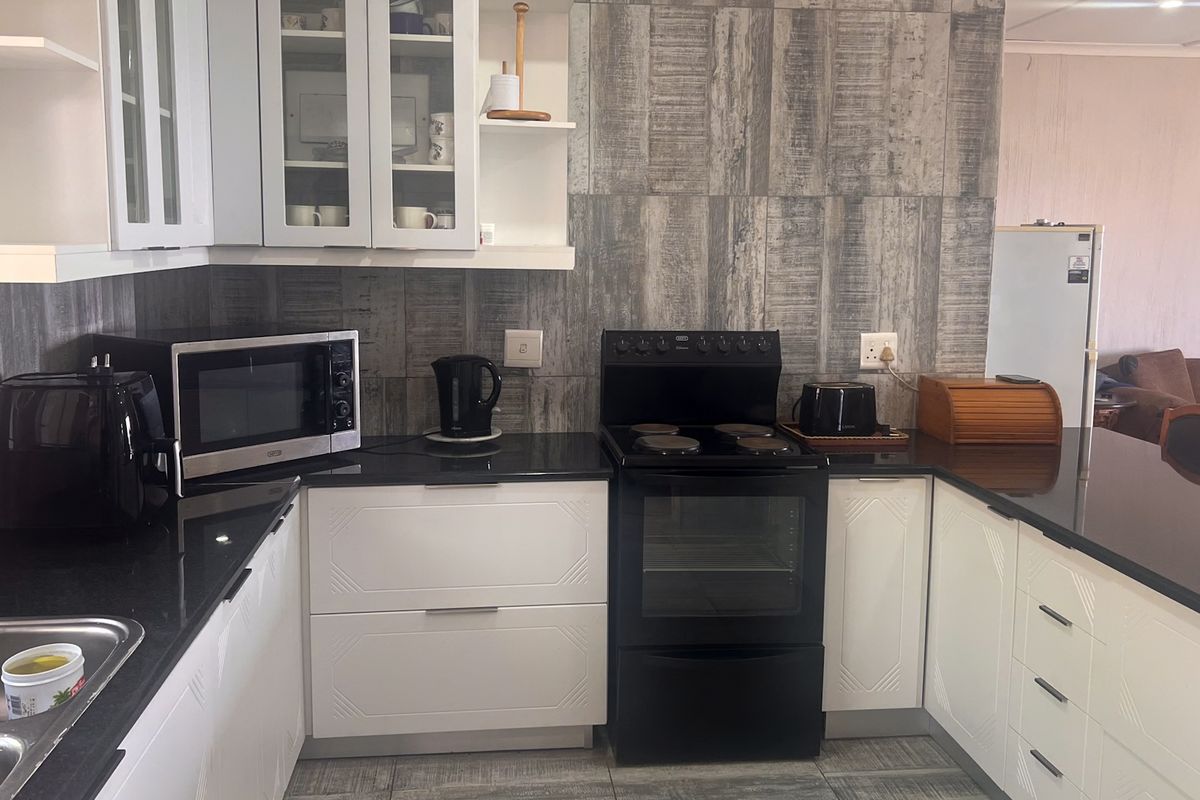 A functional kitchen featuring white cabinetry, black granite countertops, a tiled backsplash, and a freestanding electric stove.