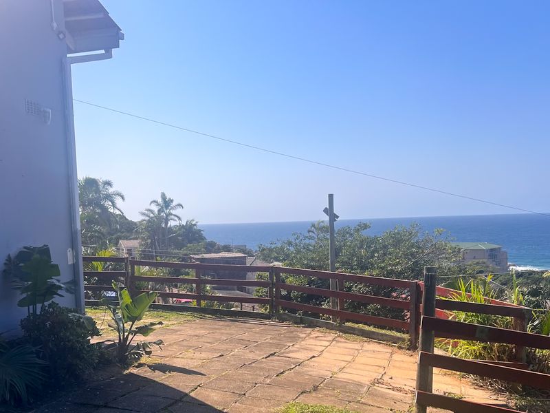 Rear exterior area featuring a paved patio, timber fencing, and elevated views of the ocean.