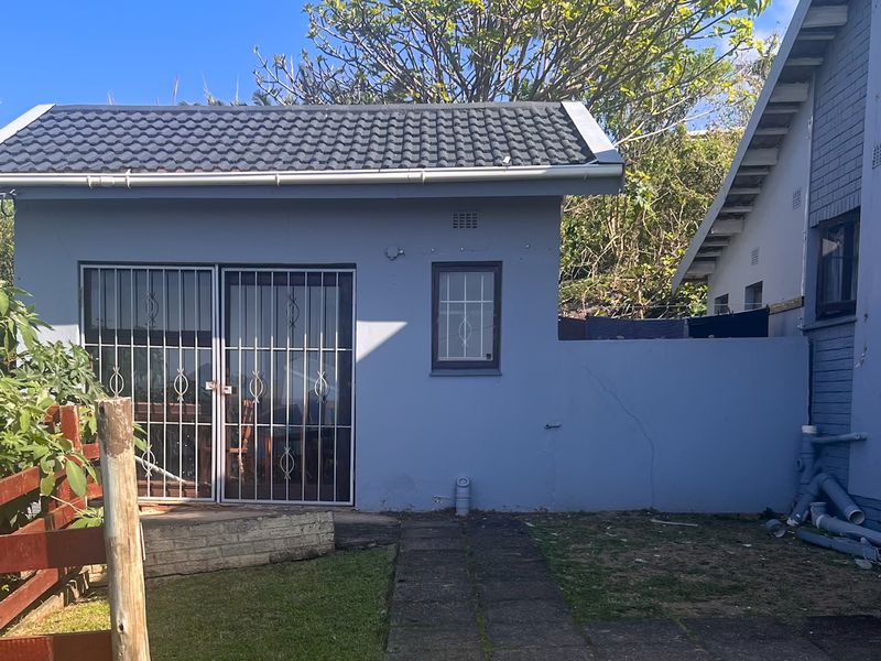 Rear view of the property showing a detached structure with a tiled roof, security gates, and a paved walkway leading to the entrance.