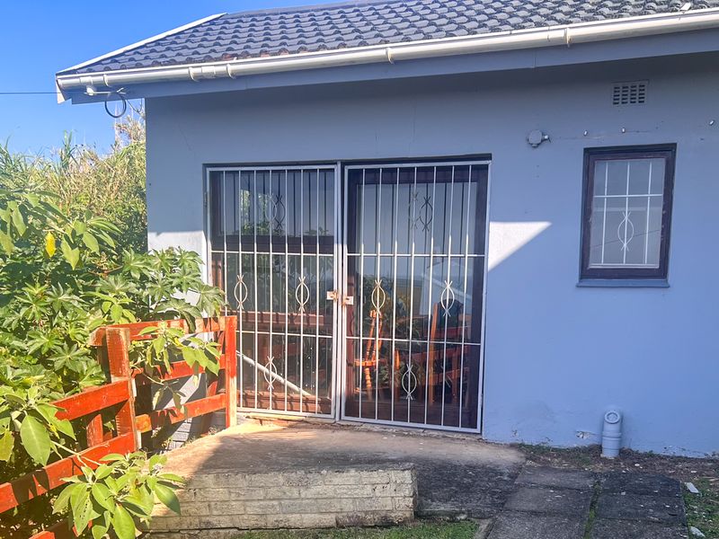 Rear exterior view of the property featuring a concrete patio, security gates, and a tiled roof structure.