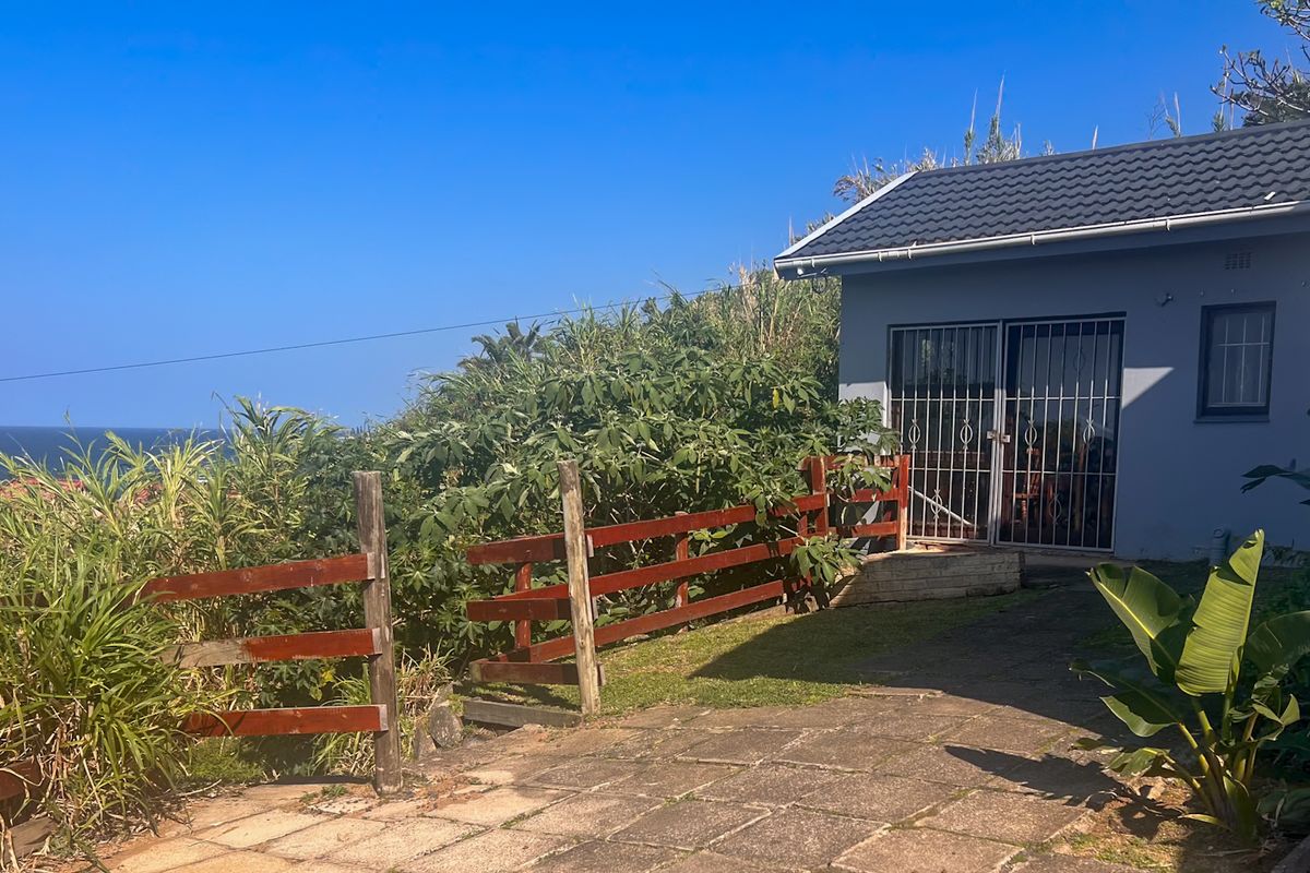 Rear exterior view of the property featuring a paved patio area, timber fencing, and a tiled roof structure with security gate access.
