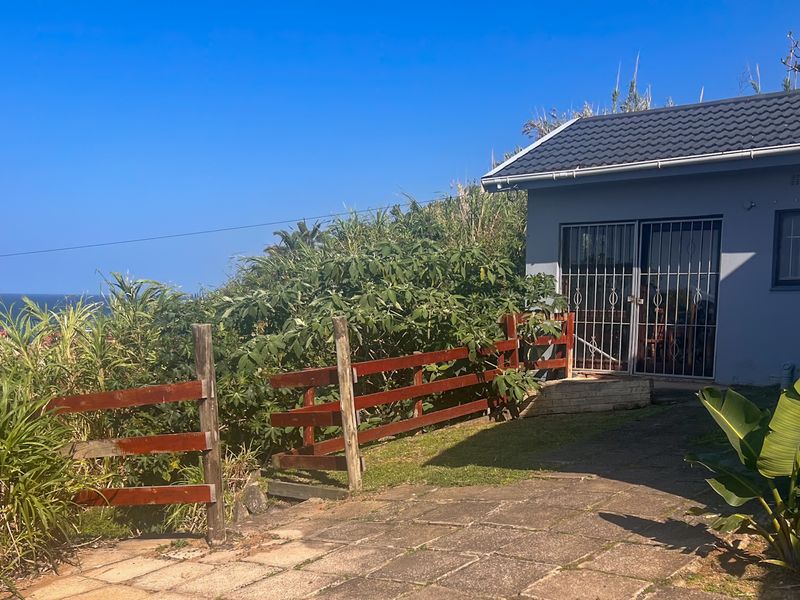 Rear exterior view of the property featuring a paved patio area, timber fencing, and a tiled roof structure with security gate access.
