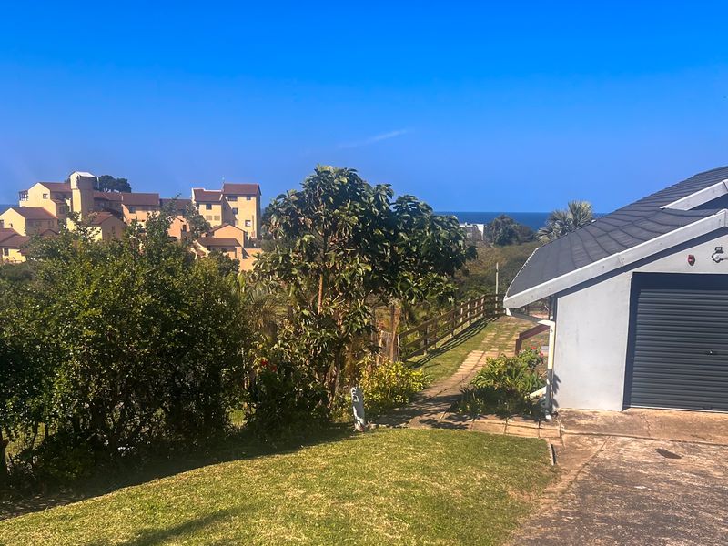 Exterior view of a residential property featuring a garage with a roller shutter door, paved driveway, and surrounding garden area with coastal views.