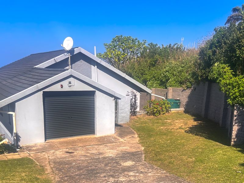 Exterior view of a residential property featuring a single garage with a roller door, concrete driveway, and surrounding garden area with boundary walls.