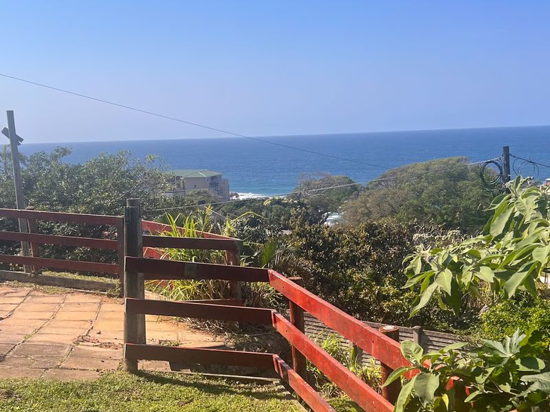 An elevated outdoor area featuring a paved patio and timber fencing, offering expansive views of the surrounding landscape and the ocean.