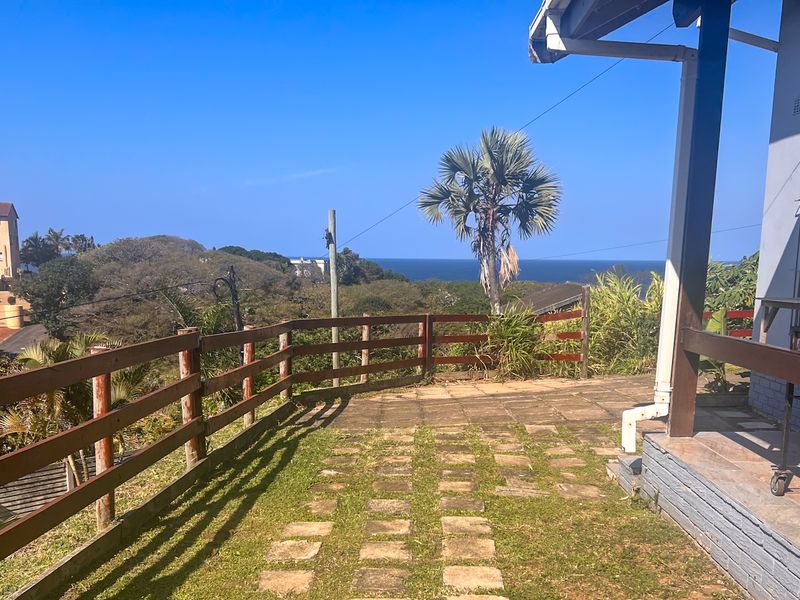 Outdoor patio area featuring a paved surface, timber fencing, and a covered veranda with scenic coastal views.