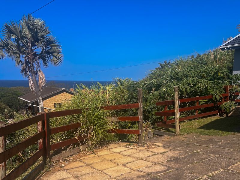 An outdoor paved patio area featuring a timber fence and views of the surrounding landscape and ocean.