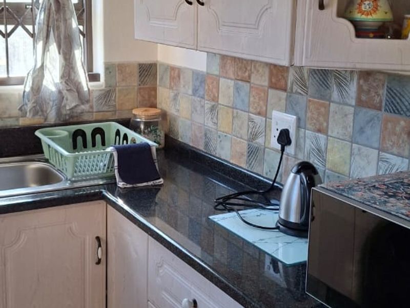 A functional kitchen featuring light-toned cabinetry, dark granite countertops, a decorative tiled backsplash, and ceramic floor tiles.