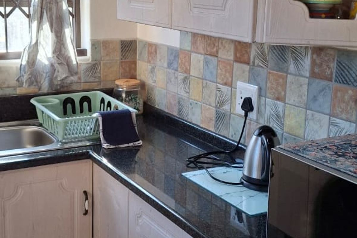 A functional kitchen featuring light-toned cabinetry, dark granite countertops, a decorative tiled backsplash, and ceramic floor tiles.
