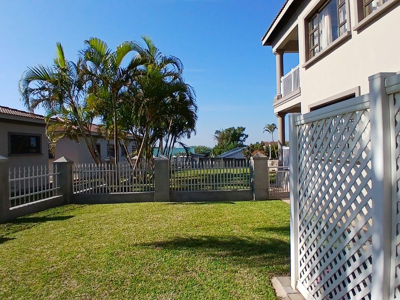 A well-maintained rear garden area featuring a manicured lawn, metal perimeter fencing with concrete pillars, and a white lattice privacy screen.
