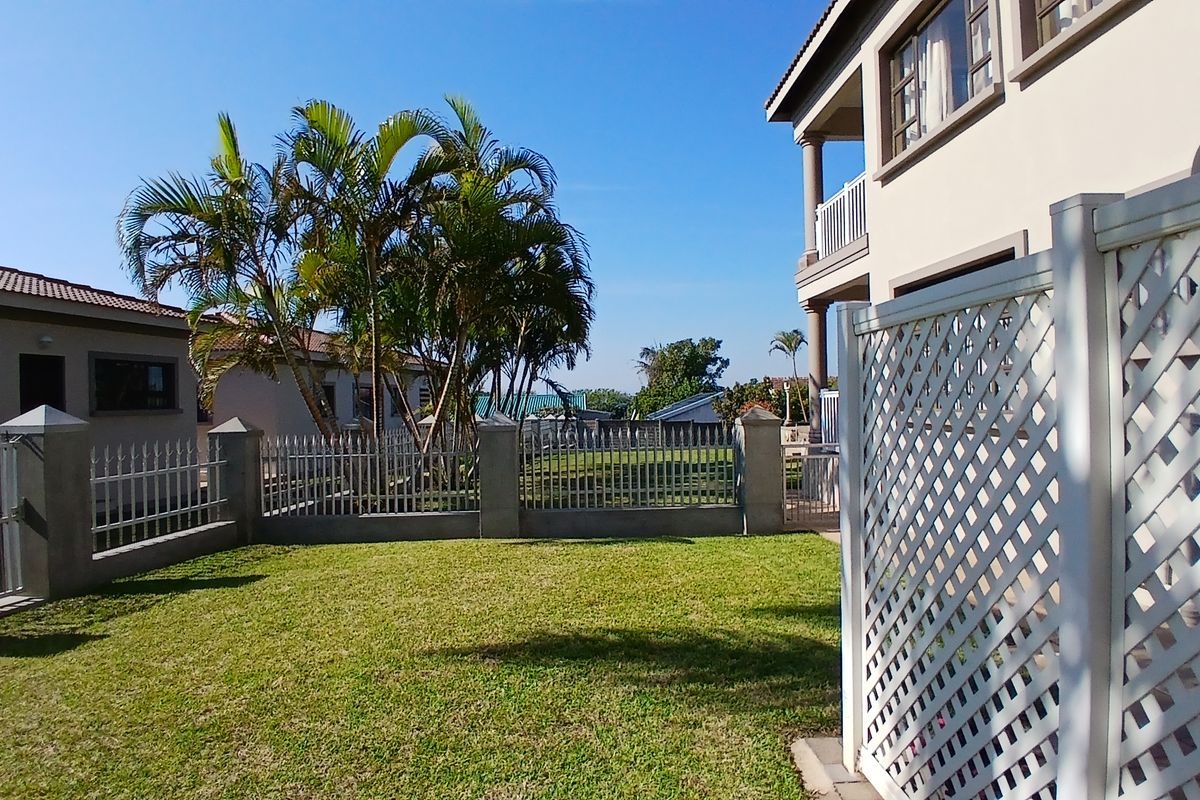 A well-maintained rear garden area featuring a manicured lawn, metal perimeter fencing with concrete pillars, and a white lattice privacy screen.
