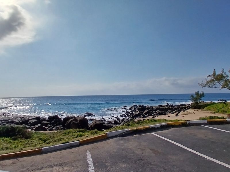 A scenic coastal view overlooking the ocean, featuring a rocky shoreline and an adjacent paved parking area.