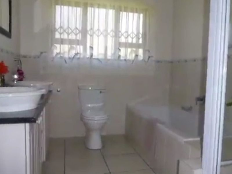 A functional bathroom featuring a double vanity, built-in bathtub, separate shower enclosure, and a window with a security gate.