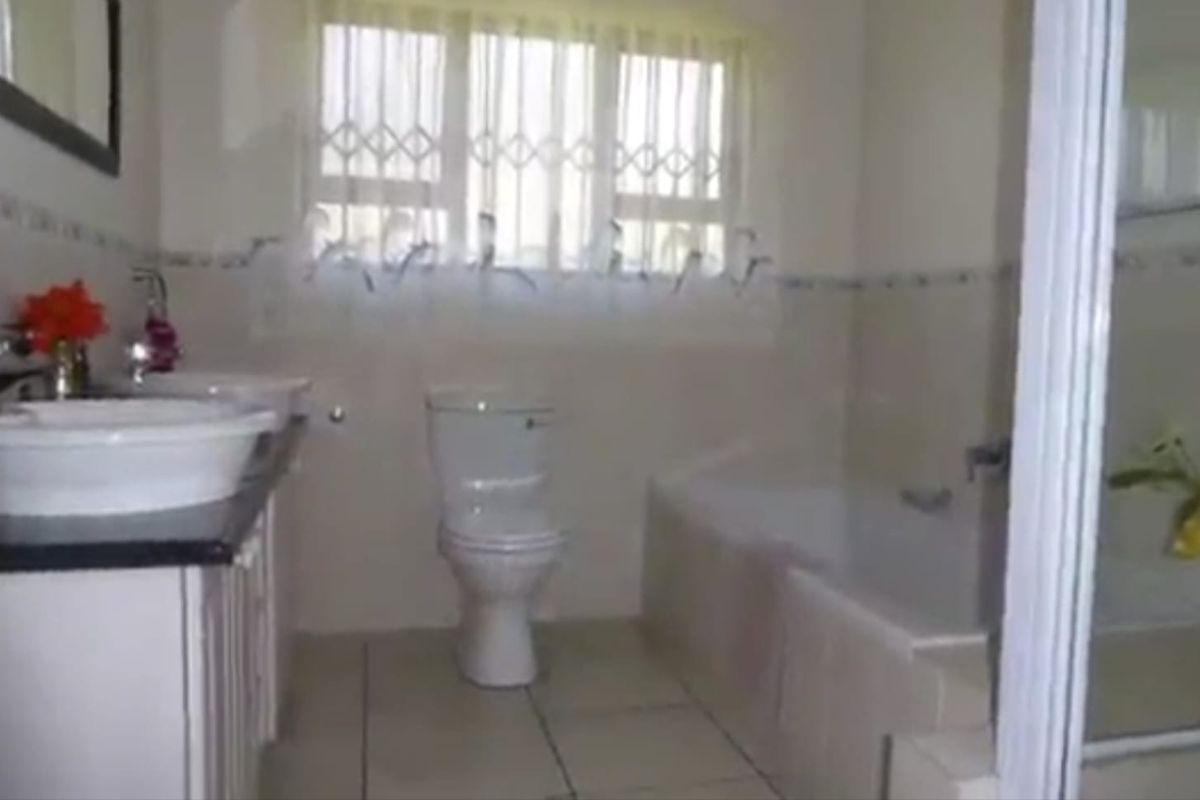 A functional bathroom featuring a double vanity, built-in bathtub, separate shower enclosure, and a window with a security gate.