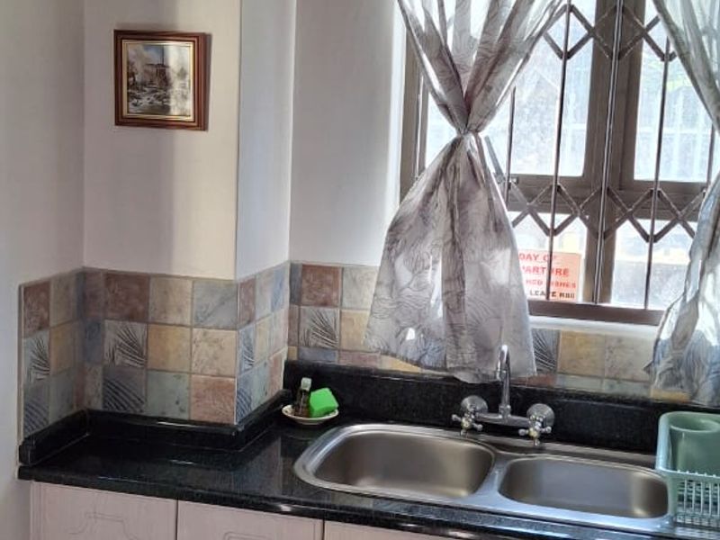 A functional kitchen area featuring granite countertops, a double basin stainless steel sink, tiled backsplash, and built-in cabinetry.