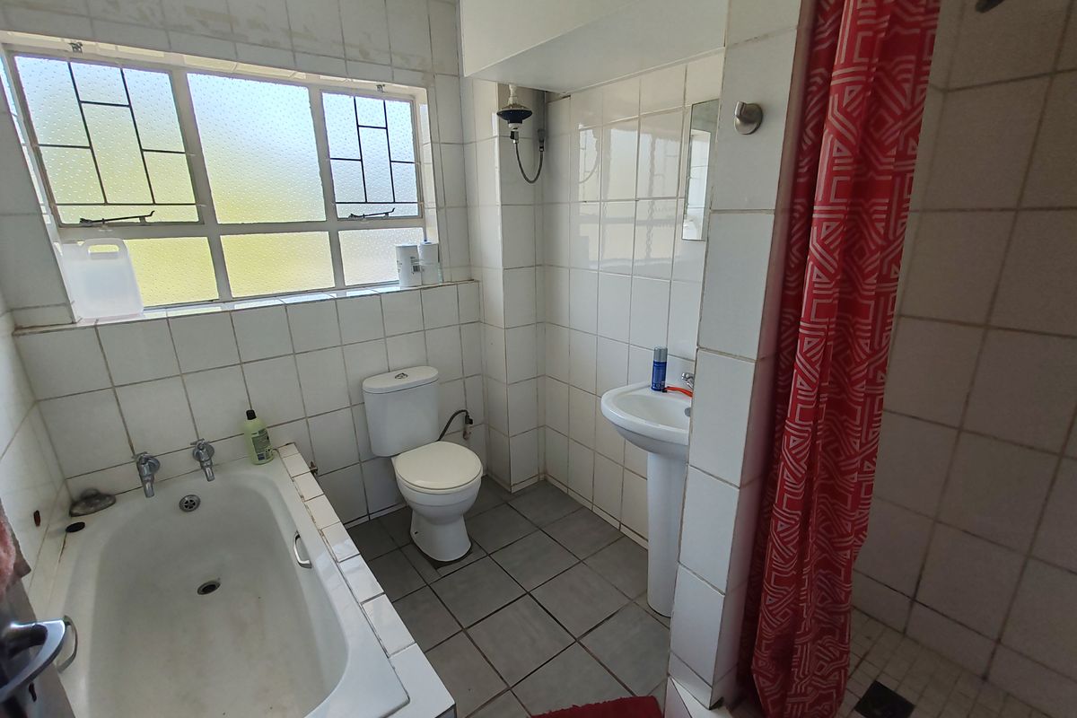 A functional bathroom featuring a bathtub, pedestal basin, toilet, and a separate shower area with tiled finishes throughout.