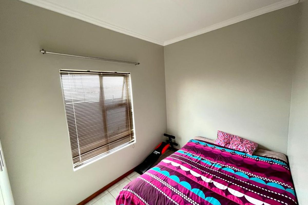 A standard bedroom featuring tiled flooring, neutral wall paint, and a window fitted with horizontal blinds.