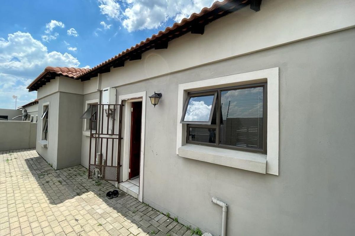 Rear exterior view of the townhouse featuring paved courtyard area, tiled roof, and secure access door with wall-mounted gas geyser.