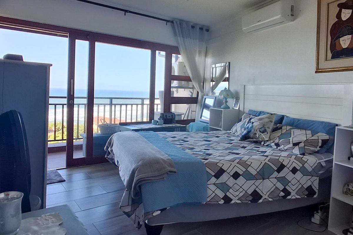 Spacious bedroom featuring tiled flooring, a wall-mounted air conditioning unit, and large sliding glass doors providing direct access to a balcony with ocean views.