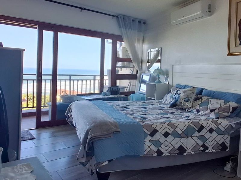 Spacious bedroom featuring tiled flooring, a wall-mounted air conditioning unit, and large sliding glass doors providing direct access to a balcony with ocean views.