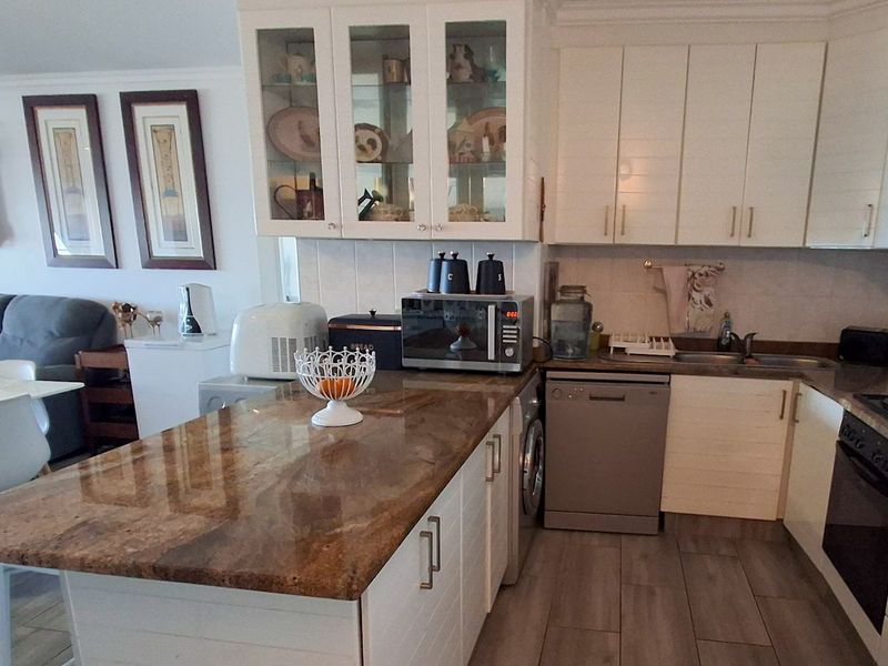 Open-plan kitchen featuring granite countertops, ample white cabinetry, built-in oven, hob, and integrated dishwasher, seamlessly flowing into the adjacent living and dining area.