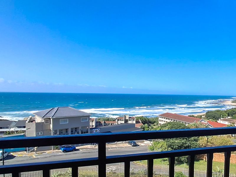 Elevated coastal view overlooking the ocean, surrounding residential buildings, and street infrastructure from a balcony.
