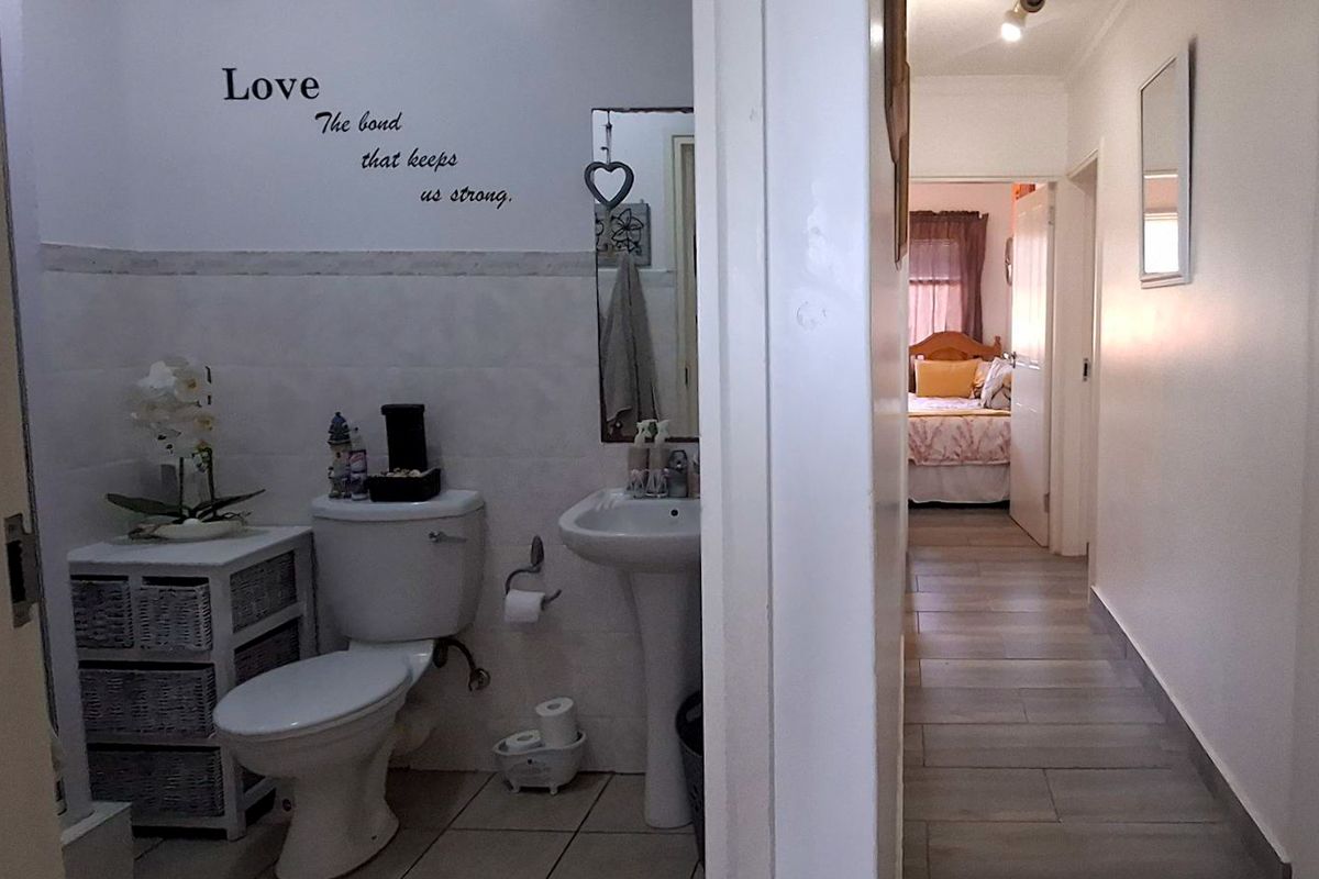 A functional bathroom featuring a pedestal basin and toilet, with tiled finishes, leading into a hallway and bedroom area.