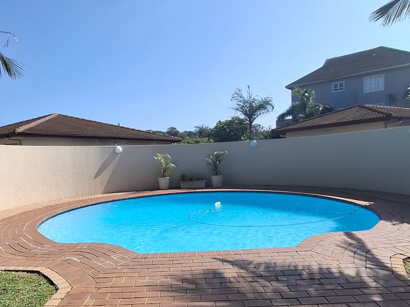 A well-maintained circular swimming pool area featuring brick paving, a curved boundary wall, and exterior wall lighting.