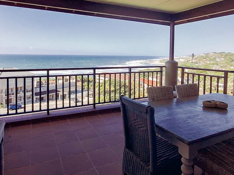 A spacious covered balcony featuring tiled flooring and a metal balustrade, offering expansive ocean and coastal views.