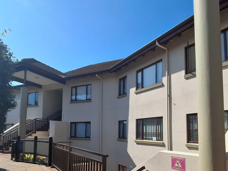 Exterior view of an apartment building featuring a tiled roof, concrete pillars, and external staircases with security railings.
