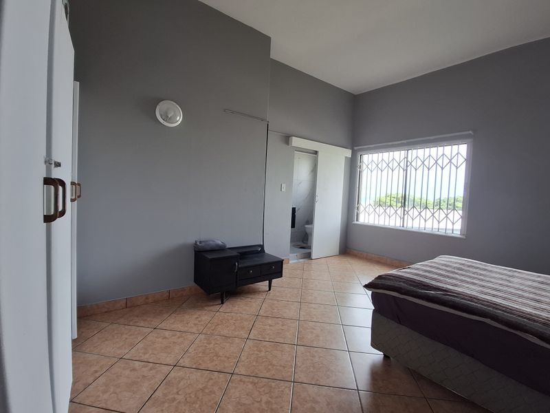 Spacious bedroom featuring tiled flooring, built-in cupboards, and a sliding door leading to an en-suite bathroom, with security bars on the window.