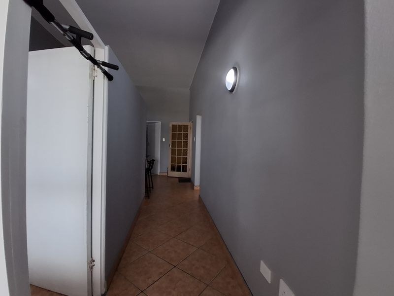 A functional hallway featuring tiled flooring, neutral grey walls, and a timber-framed glass door leading to an adjacent room.
