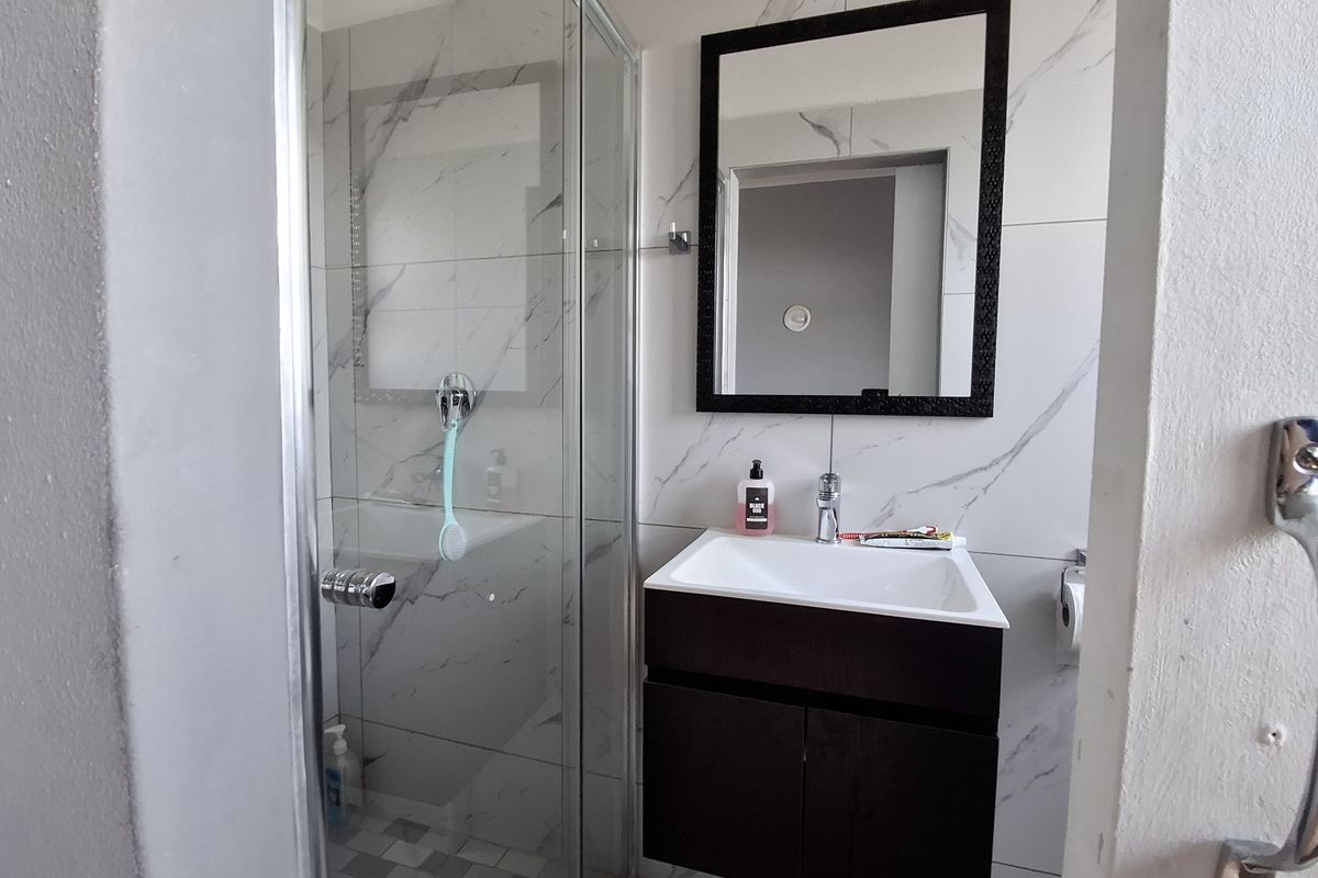 Modern bathroom featuring a glass-enclosed shower, a dark wood vanity cabinet with a white basin, and contemporary marble-effect wall tiling.