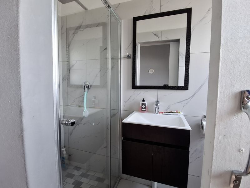 Modern bathroom featuring a glass-enclosed shower, a dark wood vanity cabinet with a white basin, and contemporary marble-effect wall tiling.