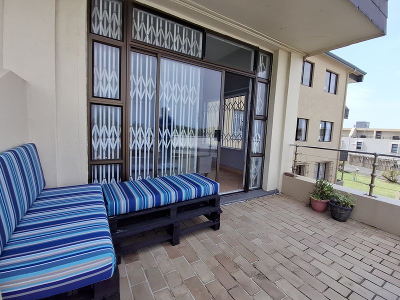 A covered balcony featuring brick paving, metal railings, and a sliding glass door with security gates, providing an outdoor living space.