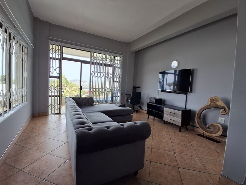 A spacious living room featuring tiled flooring, neutral grey walls, and a large sliding glass door with security gates leading to an outdoor area.