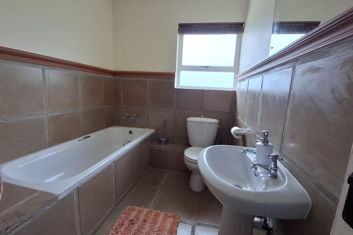 A functional bathroom featuring a bathtub, pedestal basin, and toilet with neutral tiled walls and flooring, offering a dated but well-maintained space.