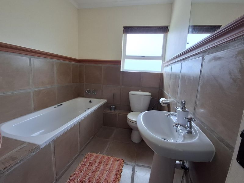 A functional bathroom featuring a bathtub, pedestal basin, and toilet with neutral tiled walls and flooring, offering a dated but well-maintained space.