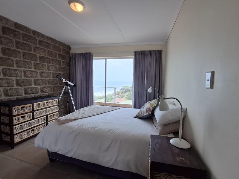 A bedroom featuring a rustic stone accent wall, tiled flooring, and a sliding glass door providing access to a balcony with coastal views.