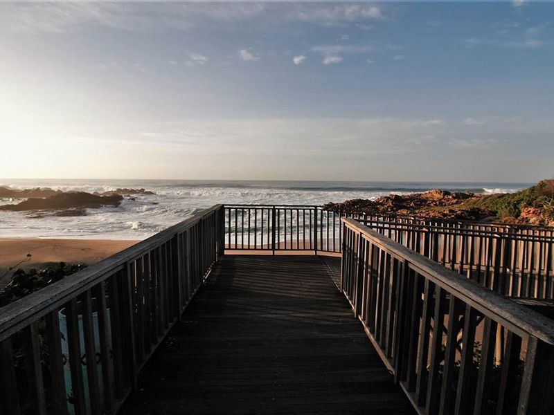 A scenic elevated timber walkway offering direct views of the coastline, ocean waves, and rocky beach shoreline.