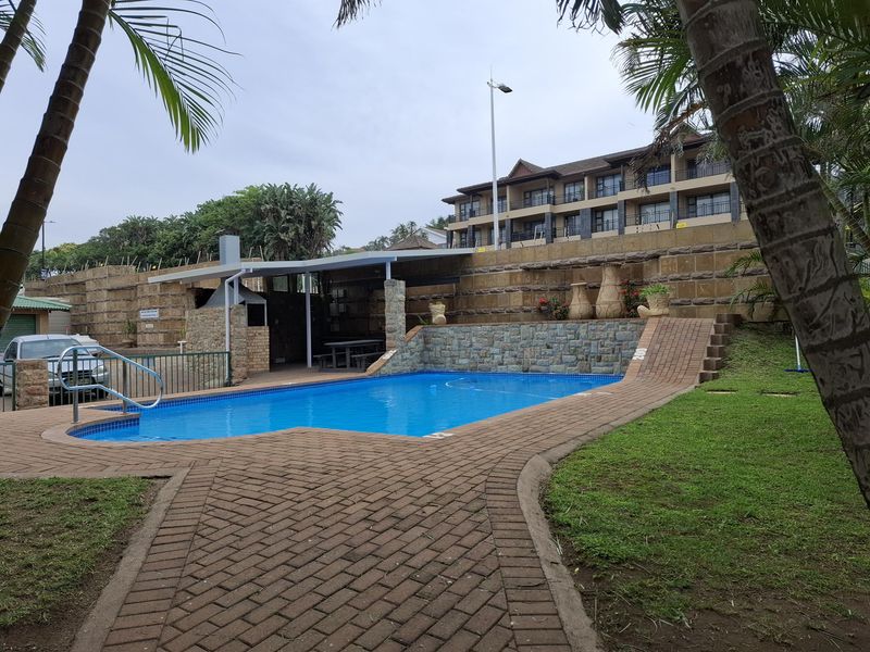 Communal swimming pool area featuring brick paving, a stone retaining wall, and a covered patio with a built-in braai facility.