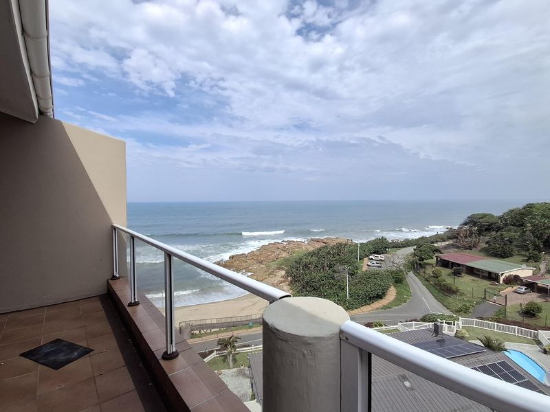 A spacious balcony featuring tiled flooring and a modern glass balustrade, offering expansive views of the coastline and ocean.
