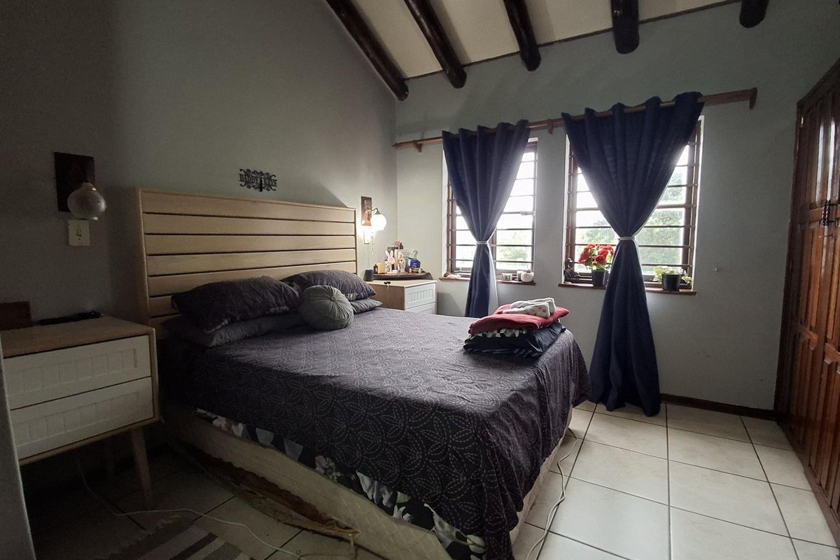 A bedroom featuring exposed timber ceiling beams, tiled flooring, and a built-in wooden wardrobe, offering a rustic aesthetic with natural light.