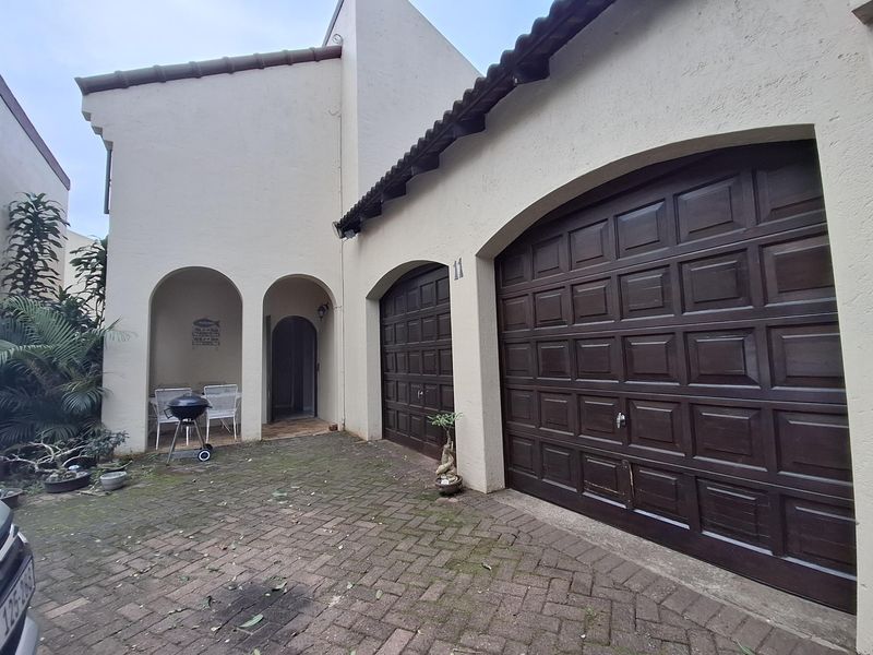 Front elevation of a townhouse featuring a double garage with dark wood-style doors, a paved driveway, and a covered entrance with arched architectural detailing.