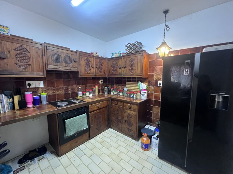 A dated kitchen featuring traditional wooden cabinetry, tiled countertops, and a tiled backsplash, offering a functional layout with built-in cooking appliances.